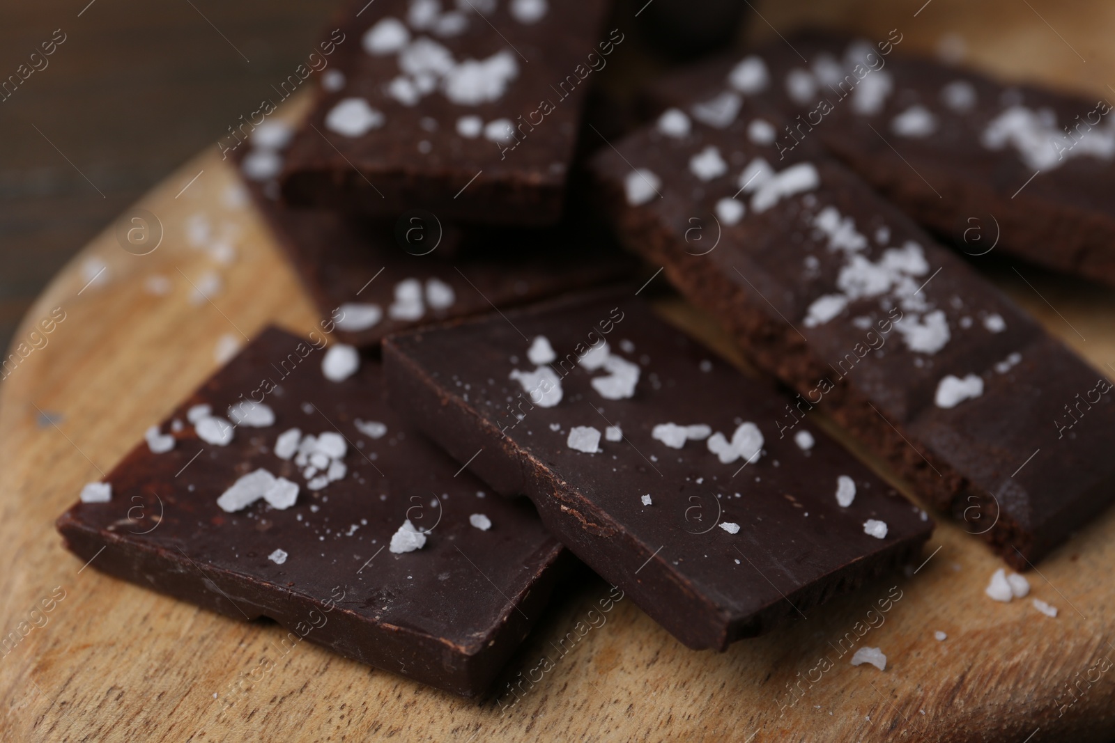 Photo of Pieces of chocolate with salt on wooden table, closeup