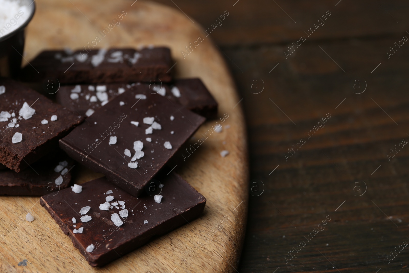 Photo of Pieces of chocolate with salt on wooden table, closeup. Space for text