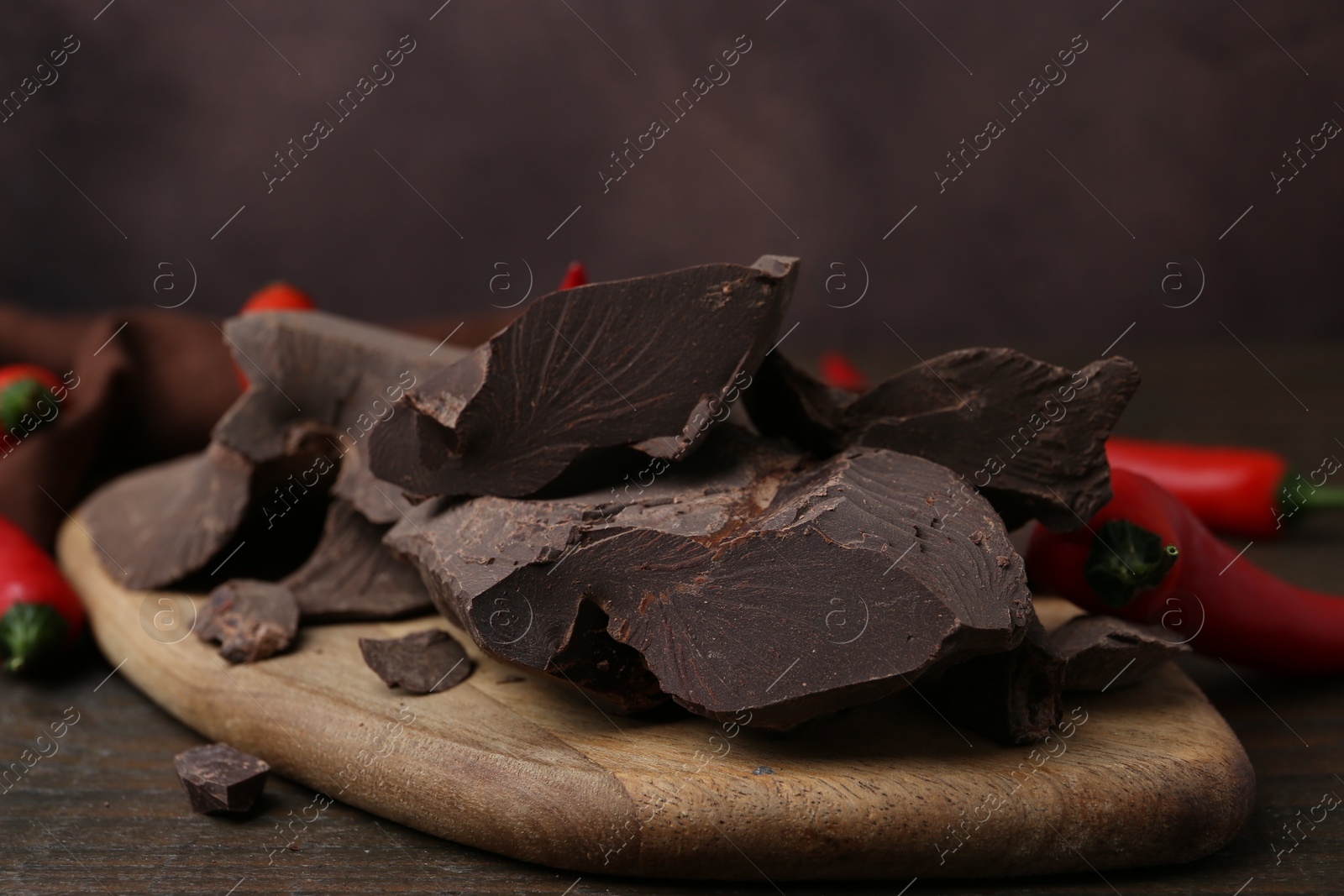 Photo of Pieces of chocolate with chili peppers on wooden table, closeup