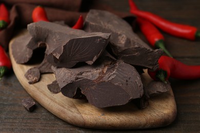 Photo of Pieces of chocolate with chili peppers on wooden table, closeup