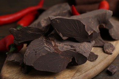 Photo of Pieces of chocolate with chili peppers on wooden table, closeup