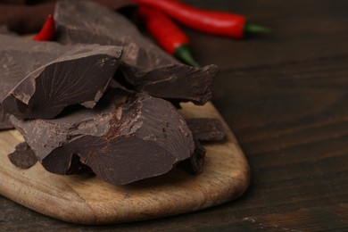 Photo of Pieces of chocolate with chili peppers on wooden table, closeup. Space for text