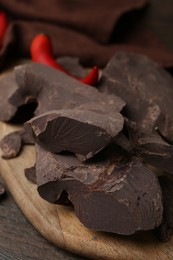 Photo of Pieces of chocolate with chili peppers on wooden table, closeup