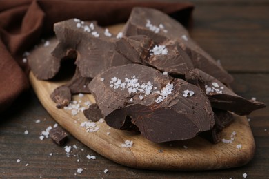 Photo of Pieces of chocolate with salt on wooden table, closeup