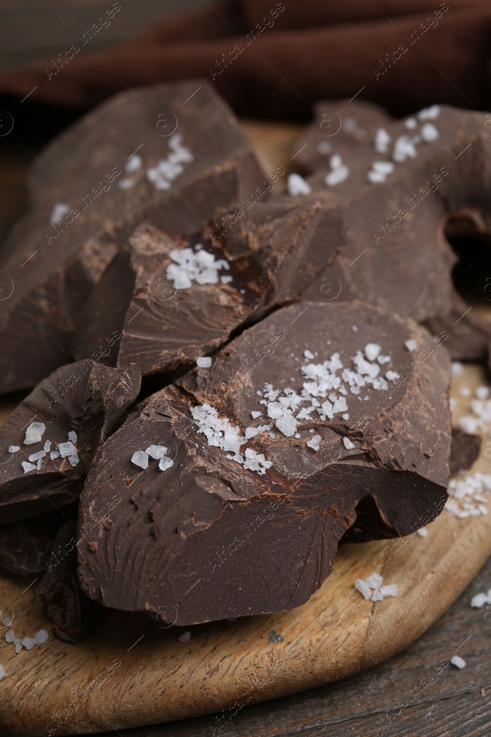 Photo of Pieces of chocolate with salt on wooden table, closeup