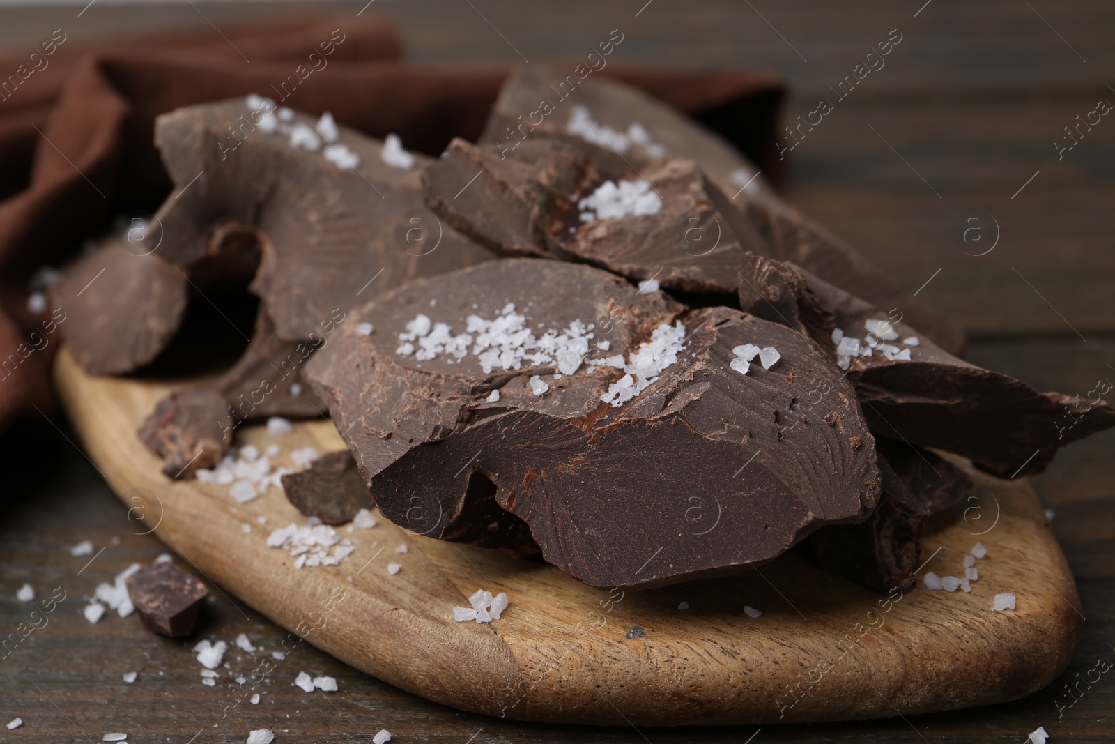 Photo of Pieces of chocolate with salt on wooden table, closeup