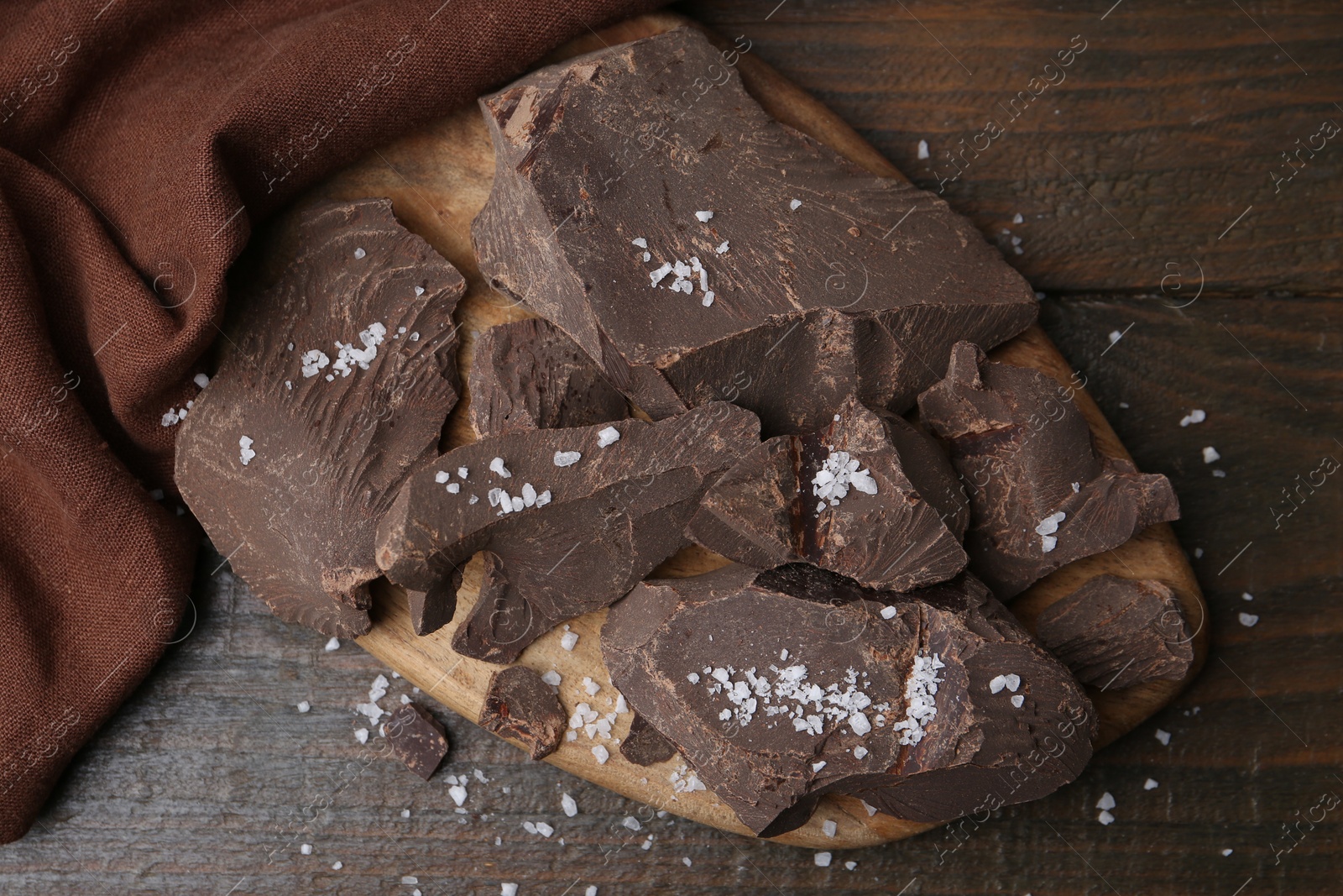 Photo of Pieces of chocolate with salt on wooden table, top view