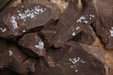 Photo of Pieces of chocolate with salt on wooden table, top view