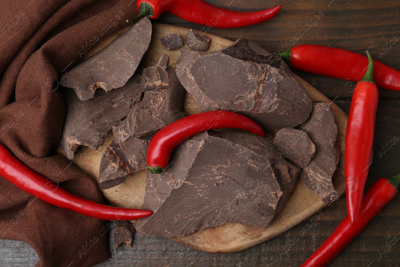 Photo of Pieces of chocolate with chili peppers on wooden table, flat lay