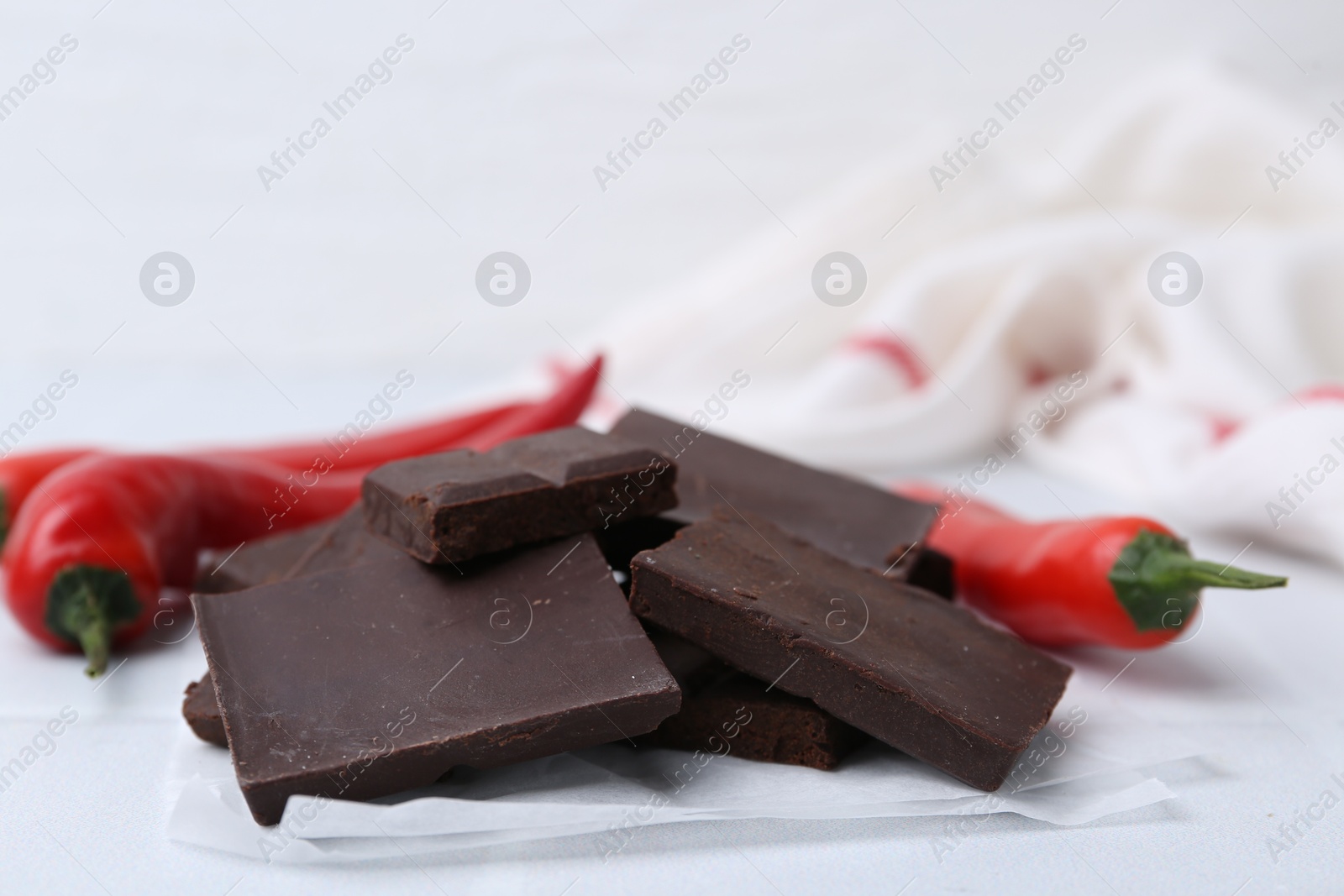 Photo of Pieces of chocolate with chili peppers on white table, closeup