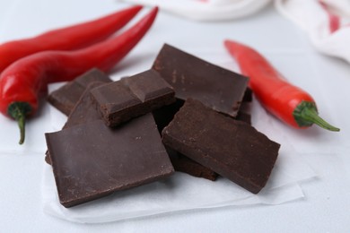 Photo of Pieces of chocolate with chili peppers on white table, closeup