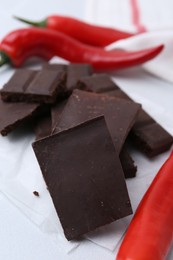 Photo of Pieces of chocolate with chili peppers on white table, closeup