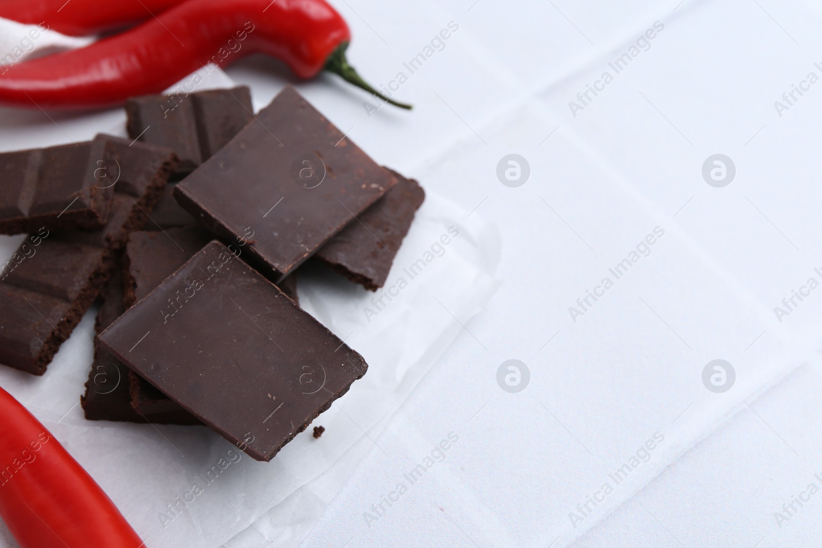 Photo of Pieces of chocolate with chili peppers on white table, closeup. Space for text