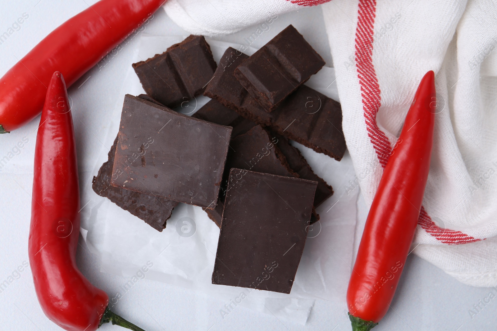 Photo of Pieces of chocolate with chili peppers on white table, above view