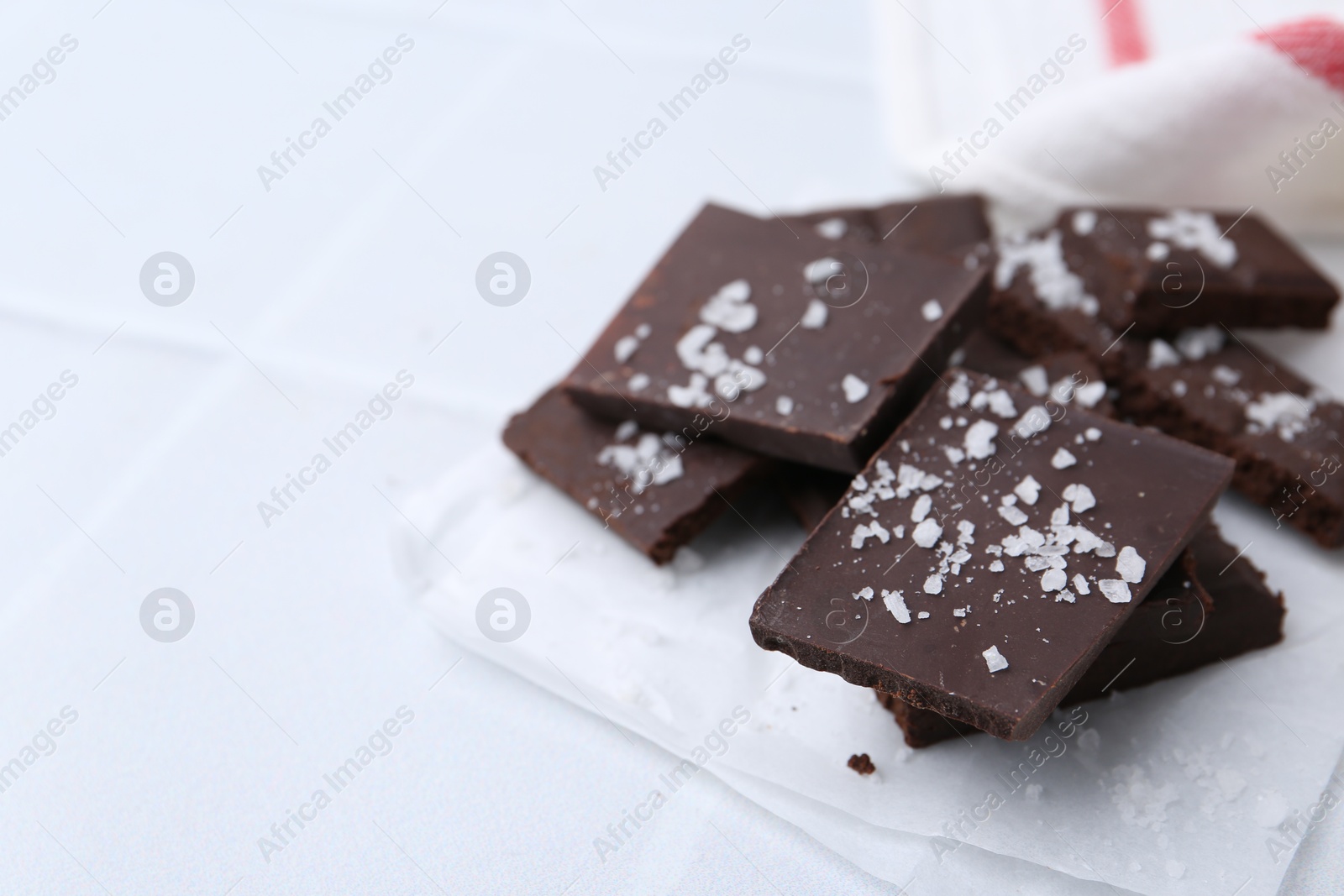 Photo of Pieces of chocolate with salt on white table, closeup. Space for text