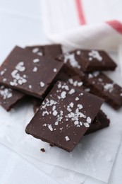 Photo of Pieces of chocolate with salt on white table, closeup