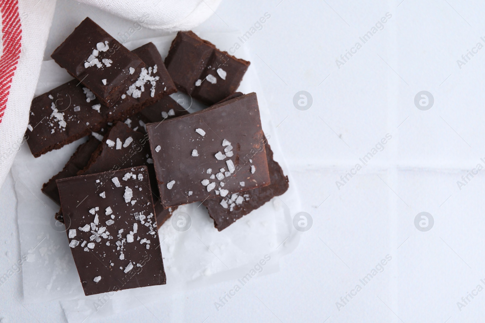 Photo of Pieces of chocolate with salt on white table, top view. Space for text