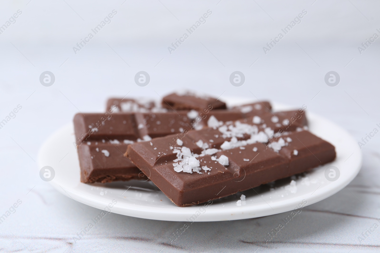 Photo of Pieces of chocolate with salt on white table, closeup