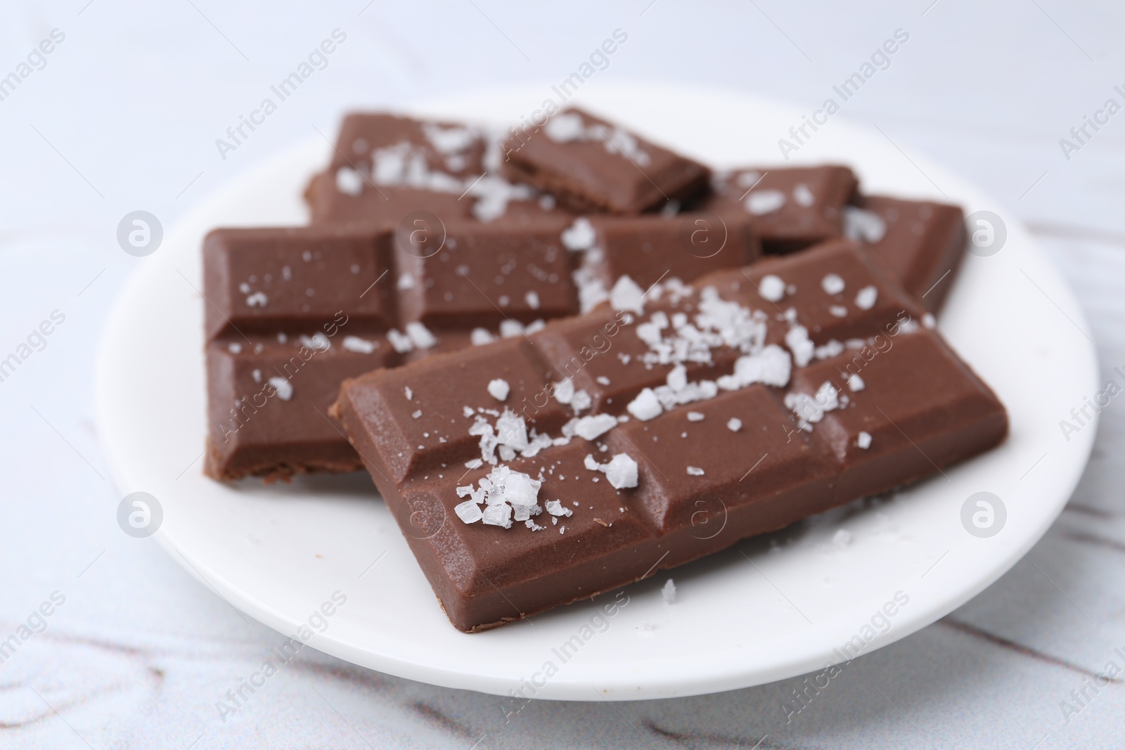 Photo of Pieces of chocolate with salt on white table, closeup