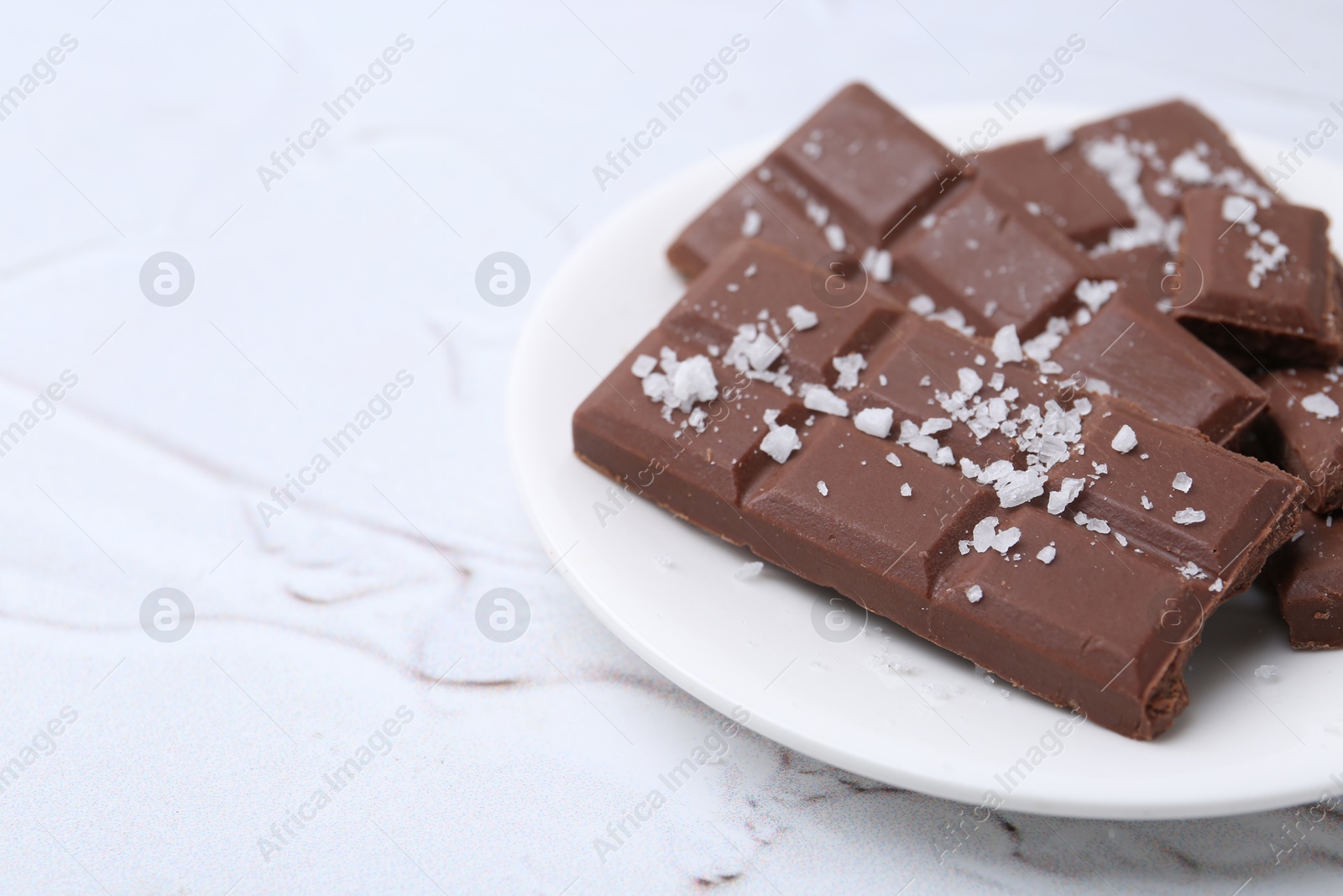 Photo of Pieces of chocolate with salt on white table, closeup. Space for text