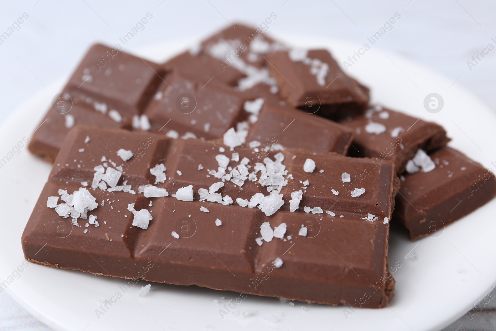 Photo of Pieces of chocolate with salt on white table, closeup