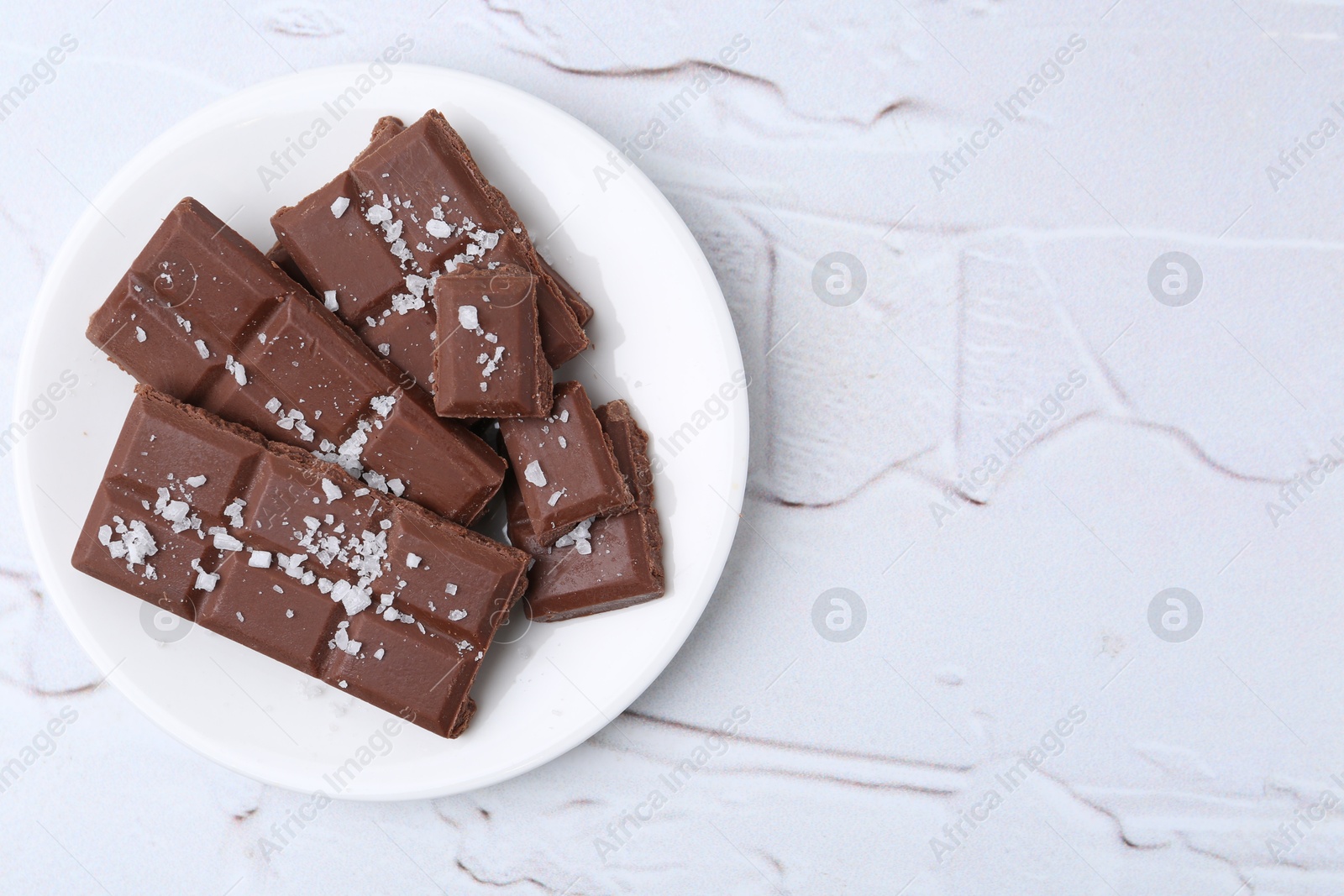 Photo of Pieces of chocolate with salt on white table, top view. Space for text