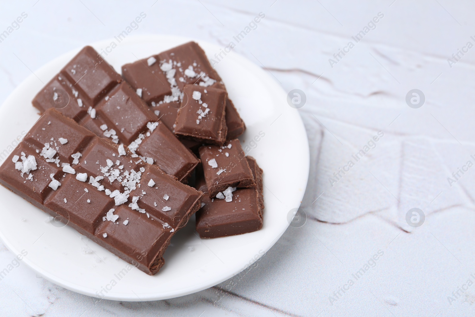 Photo of Pieces of chocolate with salt on white table