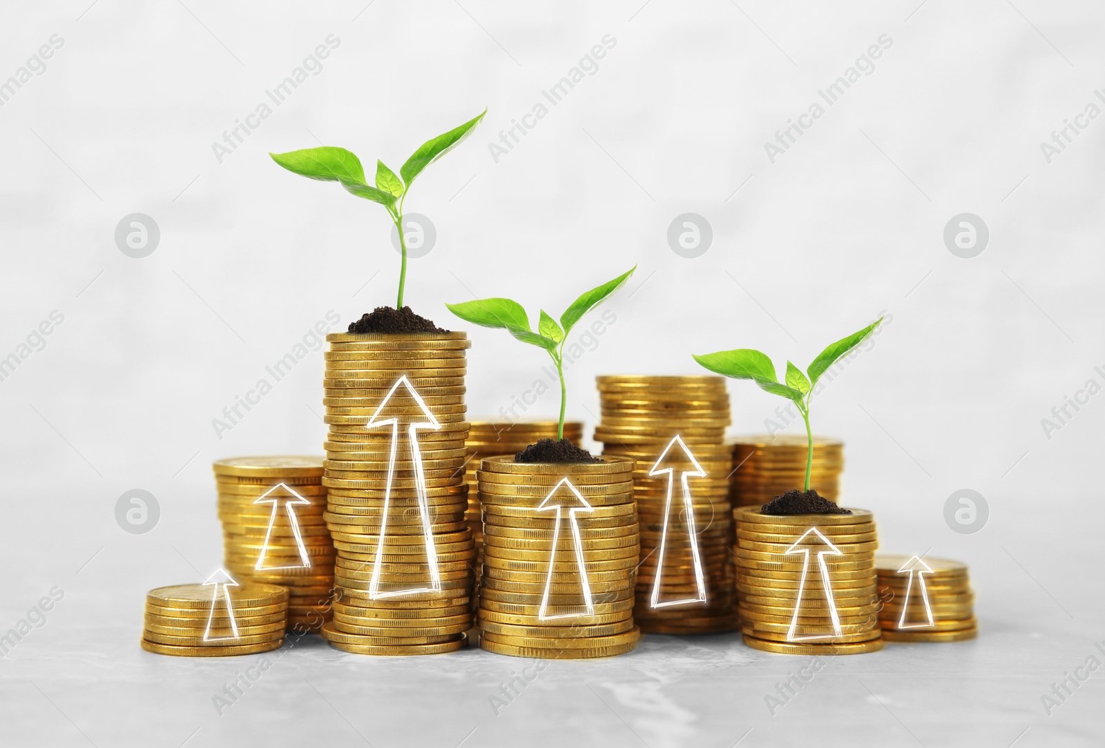 Image of Investment. Stacked coins with seedlings on tops and arrows against white background