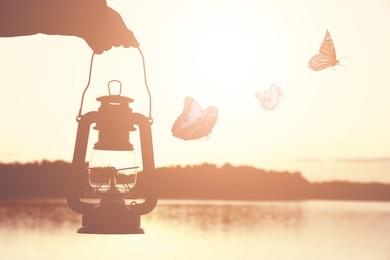 Man with vintage kerosene lamp and butterflies near river at sunset, closeup. Health, spring, freedom