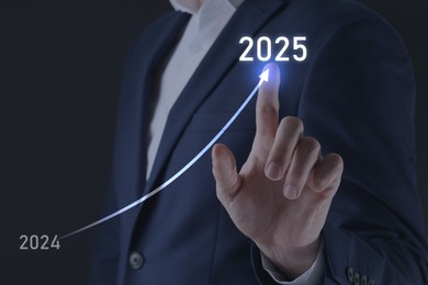 Image of New year goals. Businessman touching line leading from 2024 to 2025 on virtual screen against black background, closeup