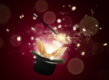 Image of Magic trick with wand. Bunny coming out of magician's hat on dark red background