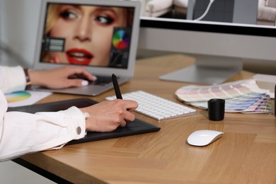 Photo of Professional retoucher working on graphic tablet and laptop at table, closeup