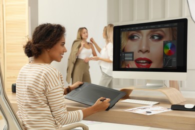 Professional African American retoucher working with graphic tablet at desk in photo studio