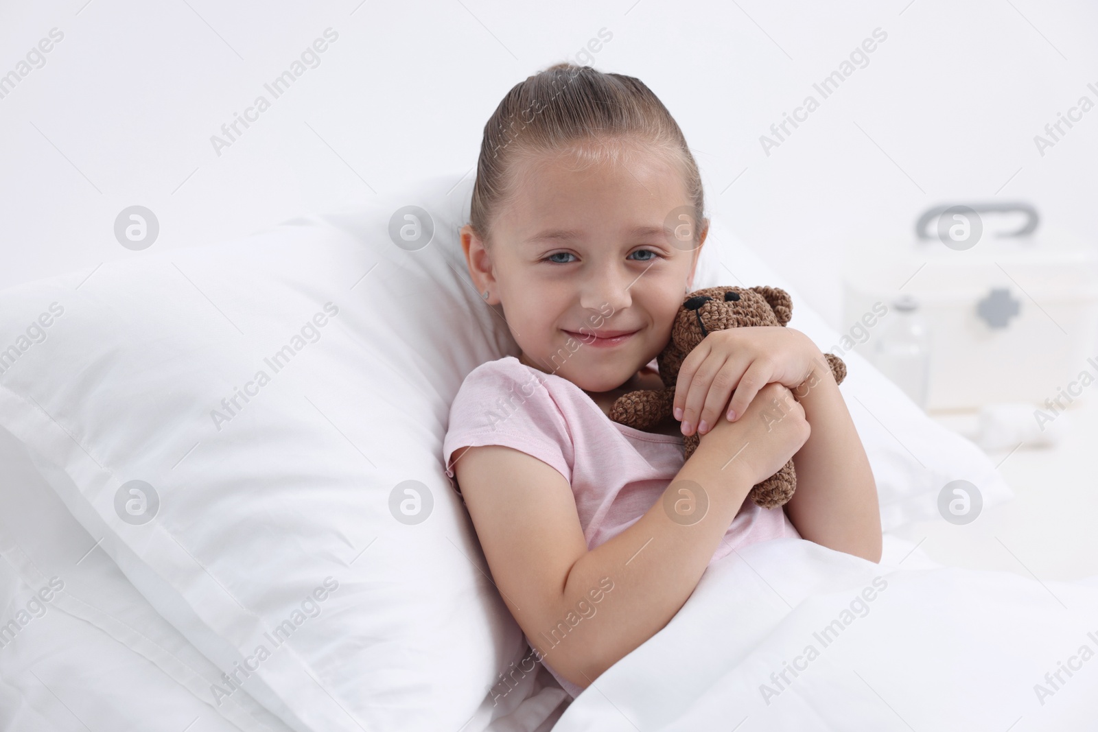 Photo of Cute little girl with teddy bear on bed in hospital