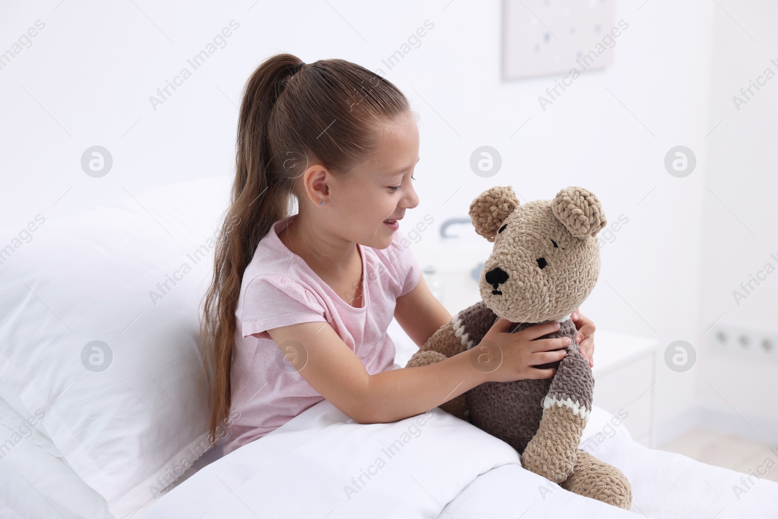 Photo of Cute little girl with teddy bear on bed in hospital