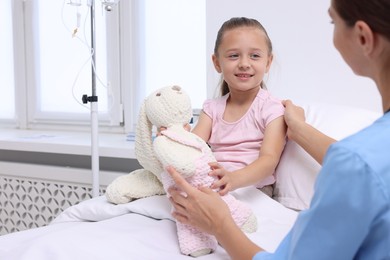 Doctor examining little girl on bed at hospital