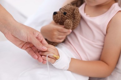 Mother and her little daughter with IV drip on bed in hospital, closeup