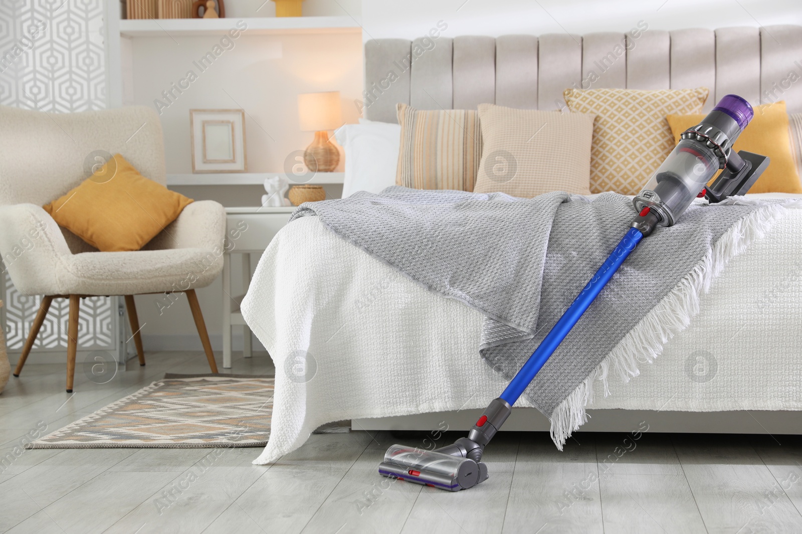 Photo of One cordless vacuum cleaner leaning on bed indoors