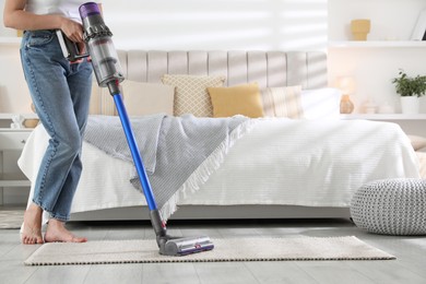 Photo of Woman cleaning rug with cordless vacuum cleaner indoors, closeup. Space for text