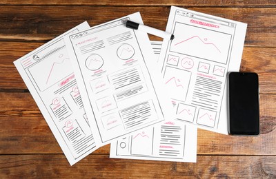 Photo of Developing UI design. Sketches of website wireframes, felt pen and smartphone on wooden table, top view