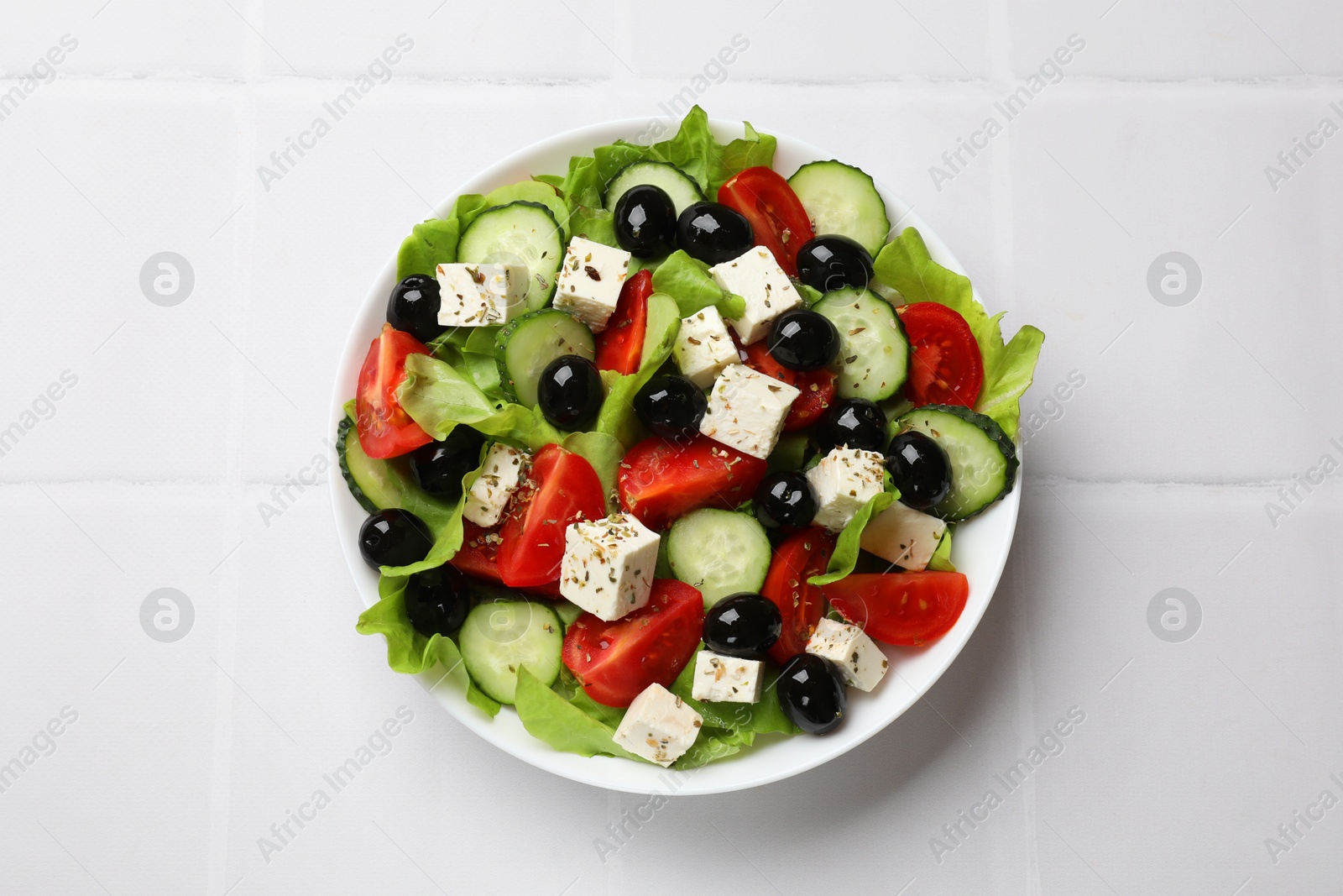 Photo of Delicious salad with feta cheese on white tiled table, top view