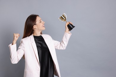 Photo of Happy winner with gold trophy cup on gray background, space for text