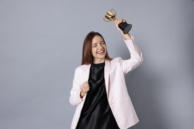 Photo of Happy winner with gold trophy cup on gray background