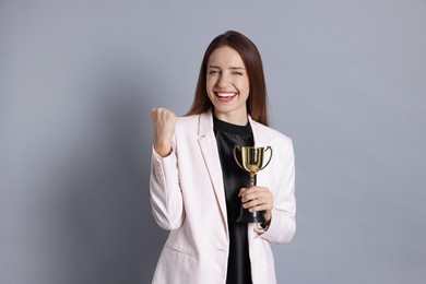 Photo of Happy winner with gold trophy cup on gray background