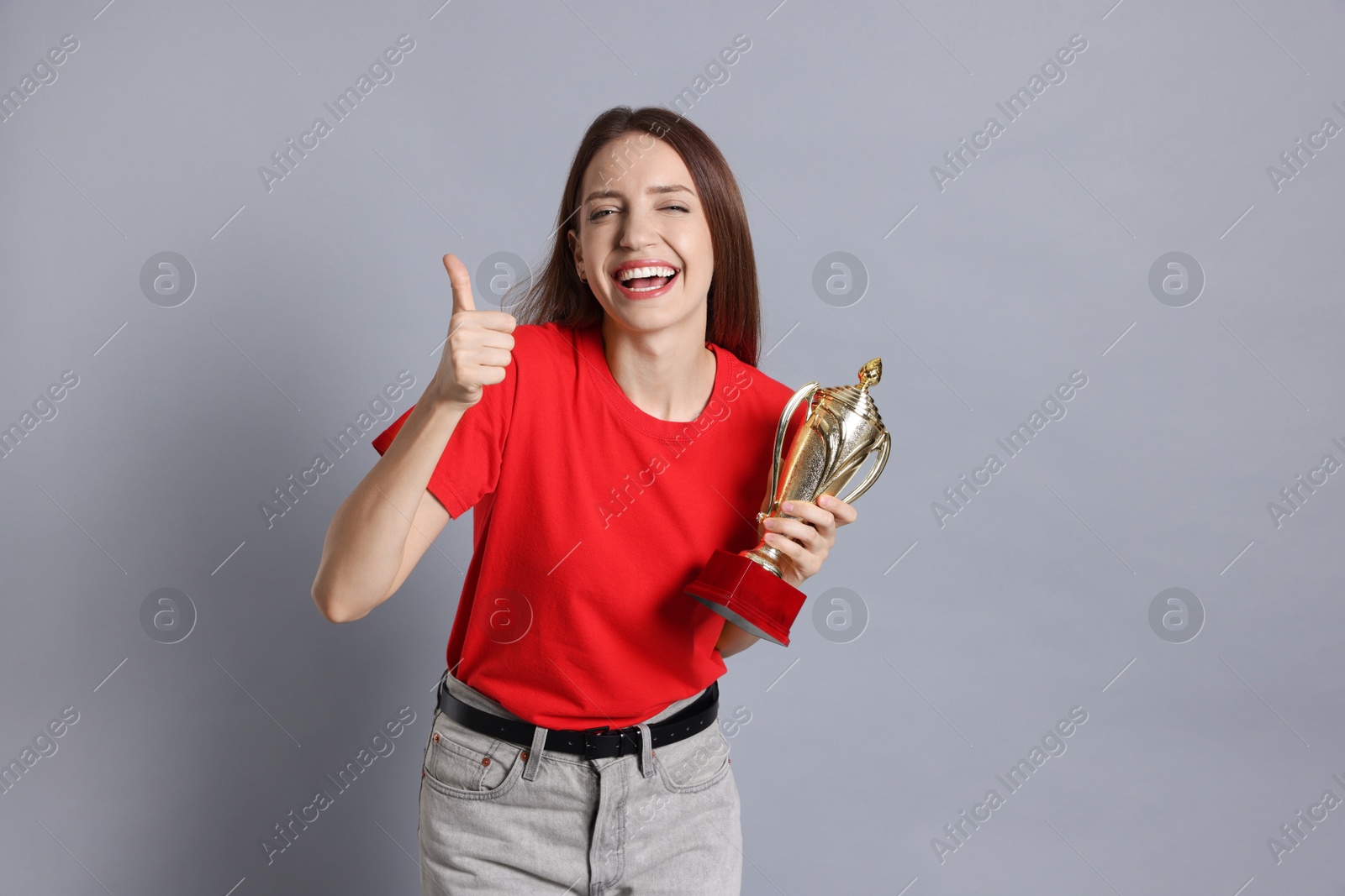 Photo of Happy winner with gold trophy cup showing thumbs up on gray background