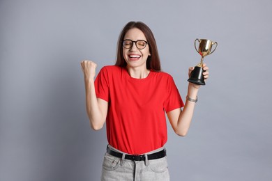 Photo of Happy winner with gold trophy cup on gray background