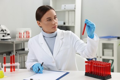 Photo of Laboratory testing. Doctor holding test tube with blood sample at table indoors