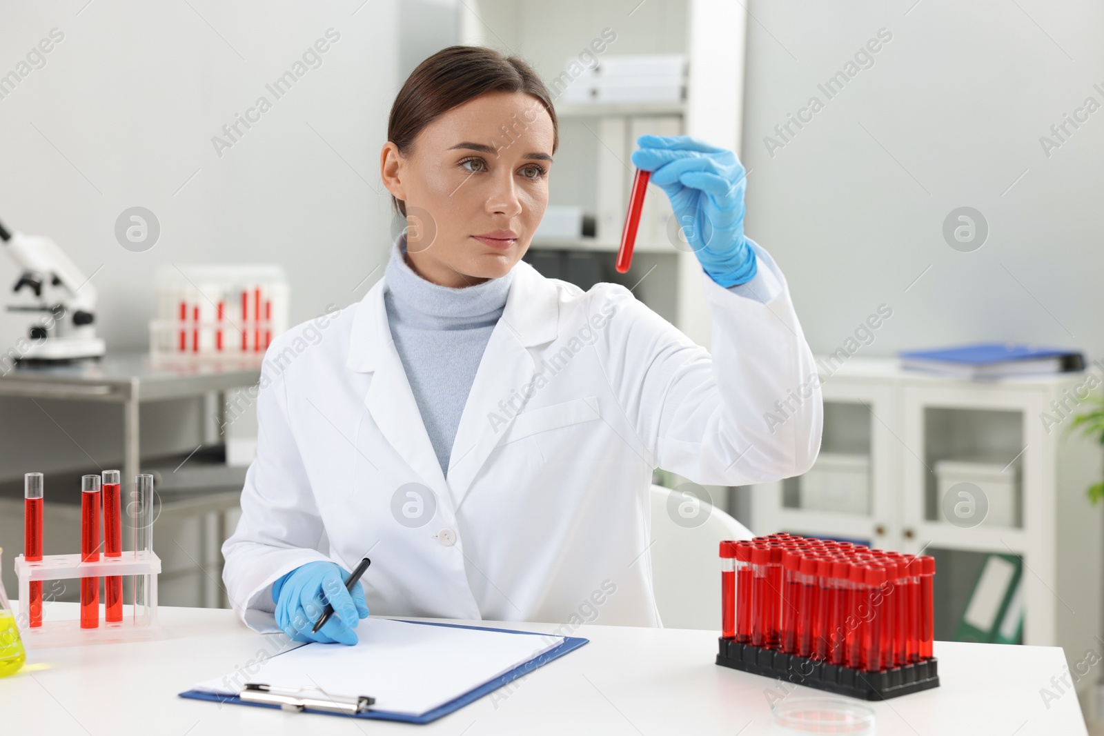 Photo of Laboratory testing. Doctor holding test tube with blood sample at table indoors