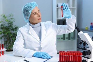 Photo of Laboratory testing. Doctor holding test tube with blood sample at table indoors