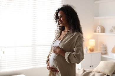 Portrait of beautiful pregnant woman near window at home, space for text